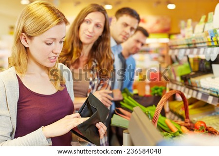 Embarrassed woman looking for money in her wallet at supermarket checkout