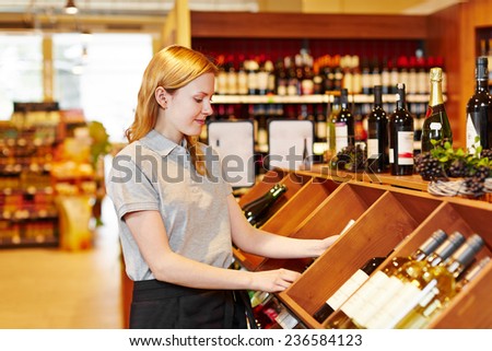 Young saleswoman in supermarket organizing bottles in wine department
