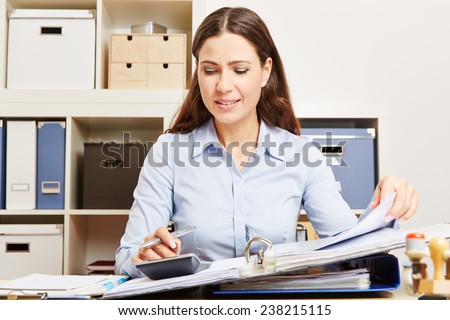 Finance clerk in office calculating financing with calculator and files