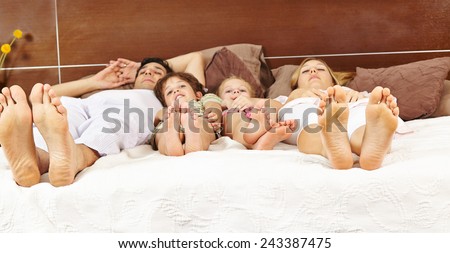Family with two children laying in bed with their feet forward