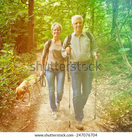 Two happy senior people walking with dog in a forest