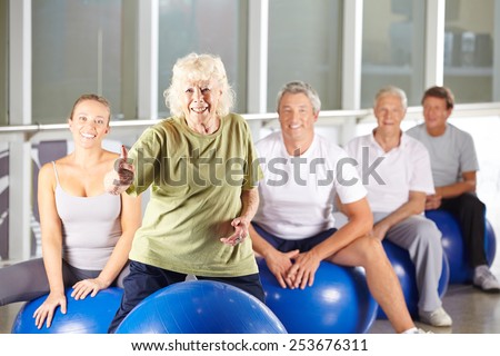 Old smiling woman in gym holding her thumbs up in fitness class