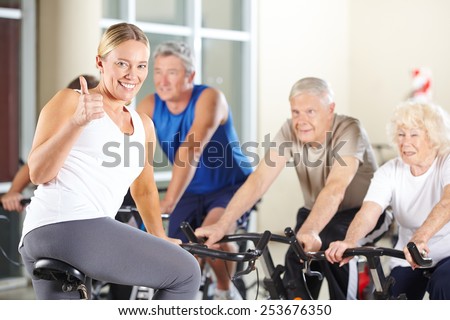 Happy fitness instructor in gym holding thumbs up with senior group
