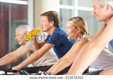 Thirsty man drinking orange juice in gym on spinning bike