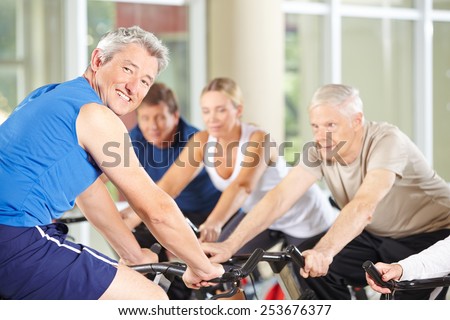 Happy fitness trainer with senior group on spinning bikes in gym