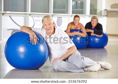 Elderly man exercising with gym ball in health club for rehab
