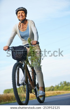 Smiling woman riding bike with helmets on a road in summer