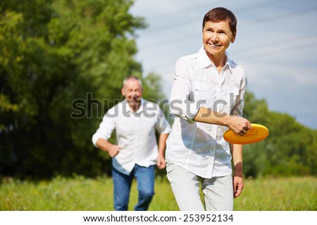 Old woman and man playing frisbee together in summer in nature