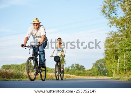 Senior couple riding bikes through summer landscape on a road