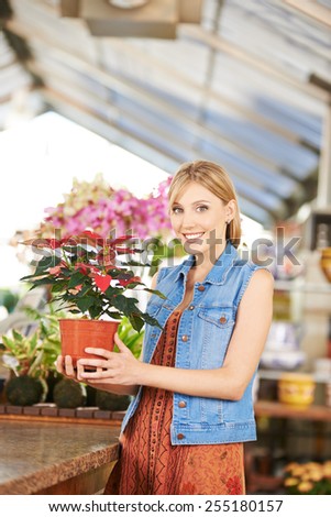 Young smiling woman buying poinsettia plant in nursery