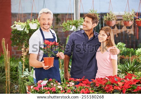 Smiling couple and a gardener in a nursery shop between plants and flowers