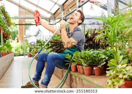 Happy gardener singing in water hose in a greenhouse of a nursery shop