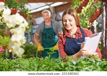 Woman with clipboard and checklist checking growth of plants in a nursery shop