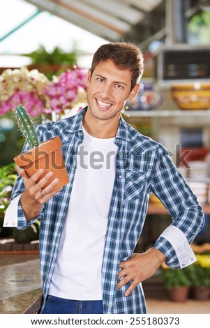 Happy gardener holding pot with cactus in a nursery shop