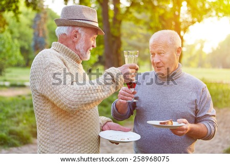 Two senior men at a birthday party cheering with glass of red wine