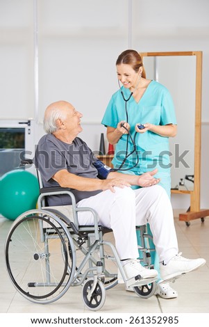 Senior man in a wheelchair getting blood pressure measurement from geriatric nurse