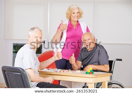 Three happy senior people in nursing home holding thumbs up and playing Bingo