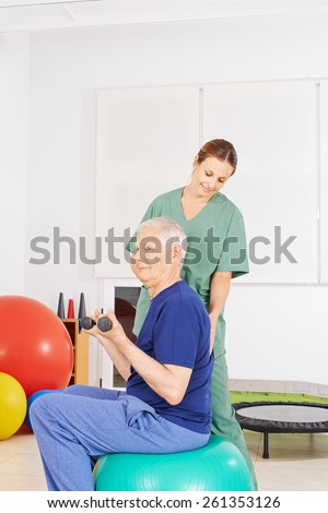 Old man with dumbbells on gym ball in a physical therapy praxis