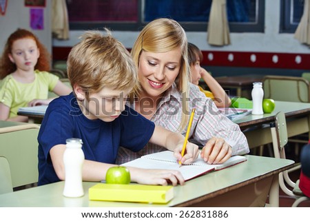 Elementary school teacher helping student in classroom at his desk