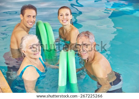 Two happy couples in aqua fitness class in a swimming pool with swim noodles