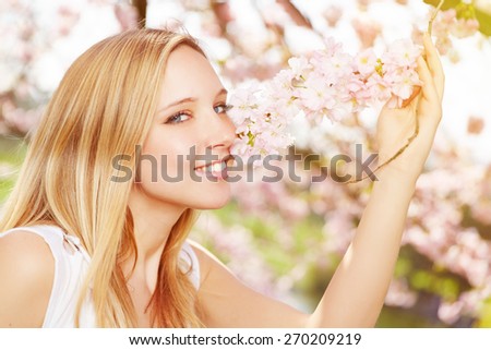 Young blonde woman smelling flavor of cherry blossom in spring