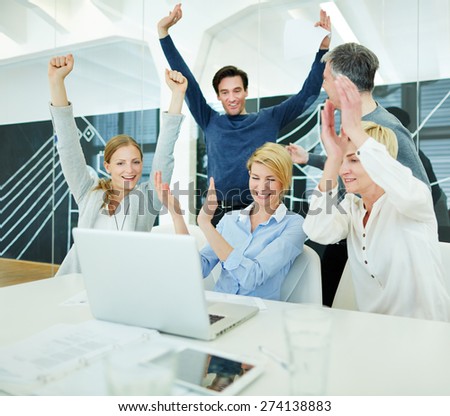 Group of happy business people cheering in office in front of computer