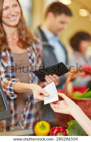 Smiling woman paying with Euro money bill at supermarket checkout