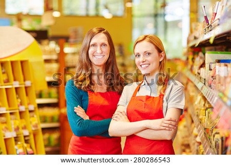 Two friendly saleswomen smiling in a supermarket with her arms crossed