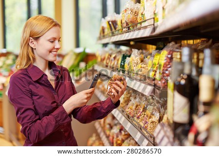 Young woman scanning barcode of bag of nuts in supermarket with her smartphone