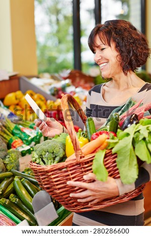 Smiling woman with shopping list buying fresh vegetables in a supermarket