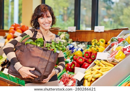 Smiling elderly woman with bag full of fresh vegetables in a supermarket