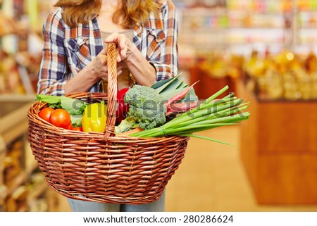 Woman carrying shopping basket full of vegetables in a supermarket
