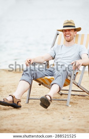 Happy man sitting relaxed in deck chair on beach in summer