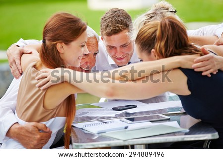 Business people hugging for team spirit in a meeting at a table