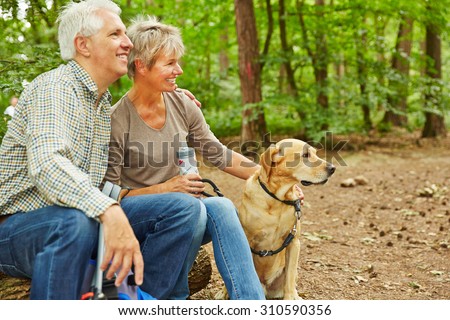 Relaxed senior couple sitting with dog in a forest during a hiking trip