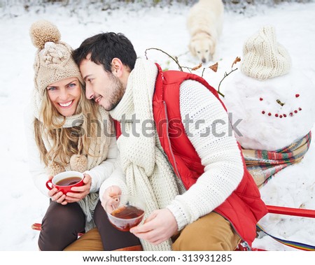Happy couple with dog drinking tea in winter sitting on a sled