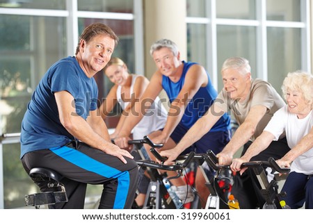 Man as fitness instructor in gym exercising with senior group in spinning class