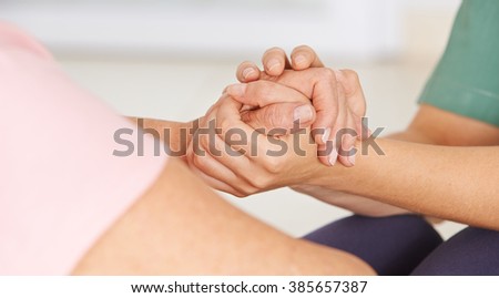 Geriatric nurse holding hands of senior woman for consolation