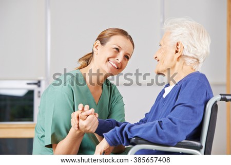 Happy geriatric nurse holding hands with senior woman in a wheelchair