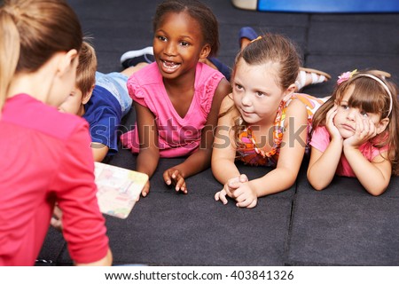 Happy children listening to fairytale book in preschool read by nursery teacher