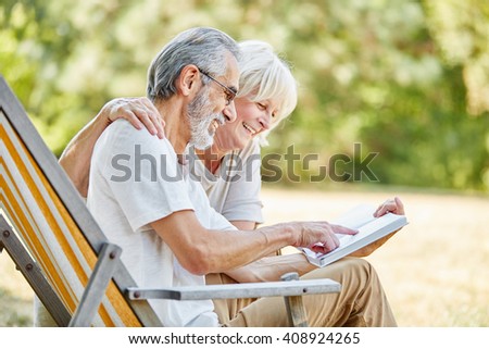 Happy seniors reading a book together in the nature in summer