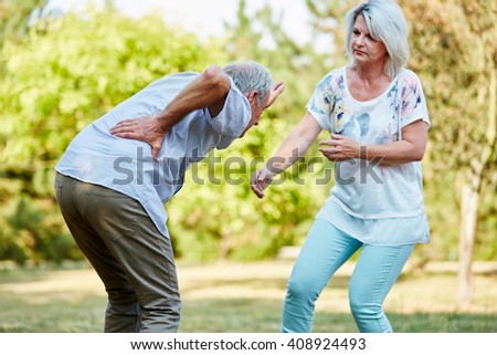 Senior woman helps man having lumbago pain in the park in summer