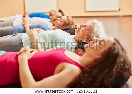 Group of people with senior relaxing  making breathing exercise at yoga class