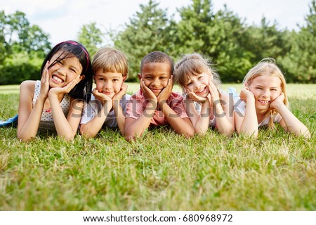 Multicultural group of children lie on grass and rest during school trip