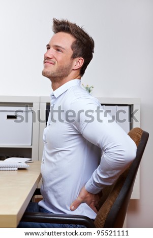 Business man with back pain in office chair at desk