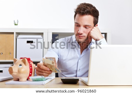 Worried business man with money and piggy bank in office