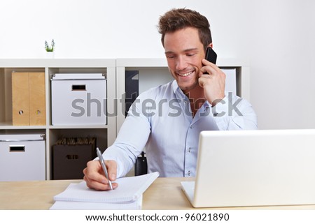 Smiling business man using cell phone at desk in office