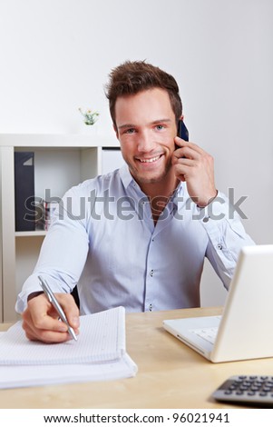 Happy business man in office making cell phone call and taking notes