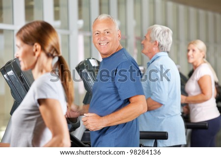 Happy senior citizens jogging on treadmills in gym