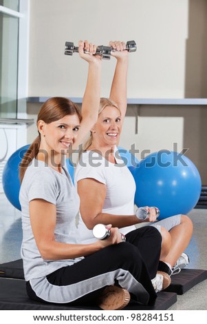 Two elderly women using dumbbells in fitness center on gym mats